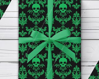 Puede incluir: Un regalo rectangular envuelto en papel negro con un patrón de damasco verde repetitivo con calaveras, atado con una cinta de satén verde brillante. El diseño incluye adornos florales que rodean cada calavera sobre un fondo negro sólido.