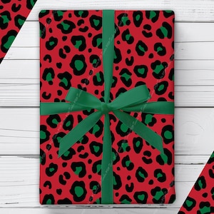 May include: A rectangular gift wrapped in red paper featuring a repeating black and green leopard print pattern. The package is tied with a dark green satin ribbon that is knotted into a bow at the center, covering the front surface of the gift.