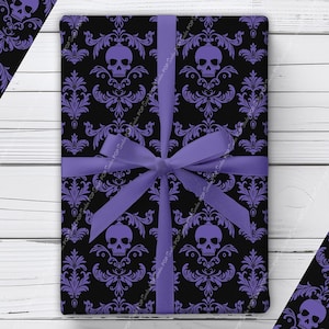 May include: A rectangular gift wrapped in black paper featuring a repeating purple damask pattern with skulls, tied with a solid light purple ribbon tied in a bow. The pattern includes ornate floral flourishes surrounding each skull design.