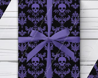 Puede incluir: Un regalo rectangular envuelto en papel negro con un patrón de damasco morado repetitivo con calaveras, atado con una cinta de color morado claro sólido en forma de lazo. El diseño incluye adornos florales alrededor de cada calavera.