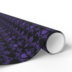 May include: Rolled sheet of black wrapping paper featuring a repeating pattern of purple skulls and floral motifs. The paper is partially unrolled, showing a white interior. The design has a gothic and spooky aesthetic.