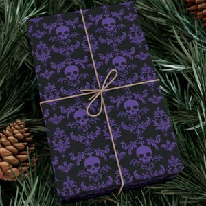 May include: A wrapped gift with black wrapping paper featuring a purple skull and damask pattern. The gift is tied with twine and set against a backdrop of pine needles and a pine cone.