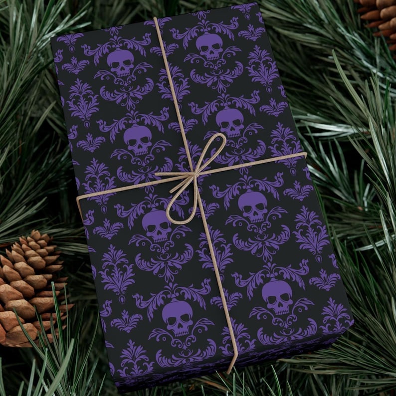 May include: A wrapped gift with black wrapping paper featuring a purple skull and damask pattern. The gift is tied with twine and set against a backdrop of pine needles and a pine cone.