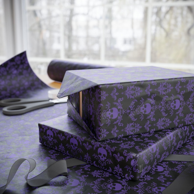 May include: Gift-wrapped boxes with black and purple skull and damask patterned paper. A roll of matching paper, scissors, and a grey ribbon are also visible, suggesting a Halloween or gothic theme.
