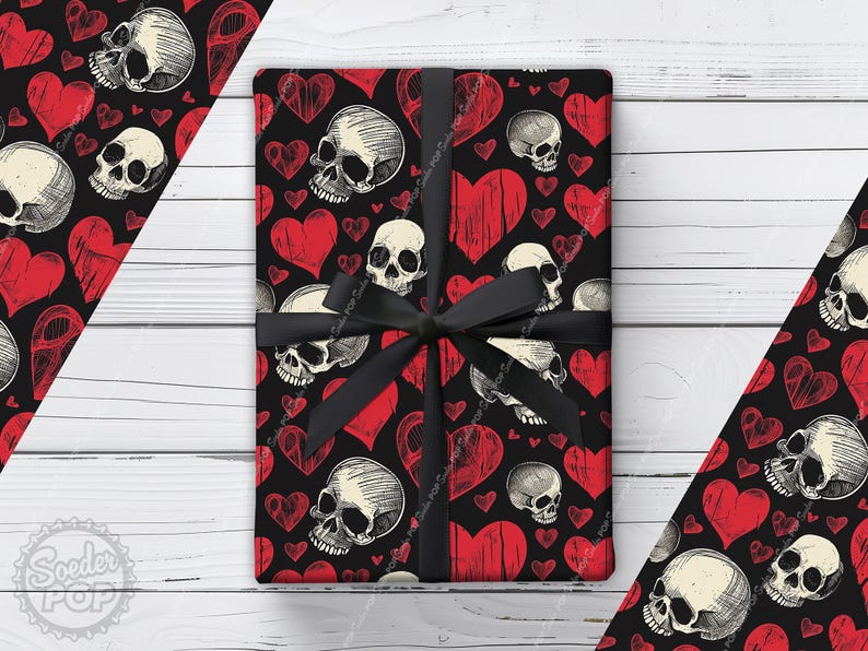 May include: A rectangular gift box wrapped in black paper featuring a repeating pattern of off-white human skulls and distressed red hearts. The package is tied with a black satin ribbon tied in a bow at the center, covering the surface.