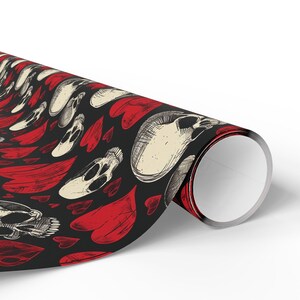 May include: A roll of wrapping paper featuring a repeating pattern of off-white human skulls and red hearts on a black background. The skulls are illustrated with fine black ink lines, and the hearts are filled with textured red shading.
