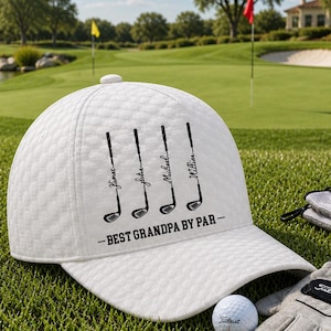 May include: A white golf cap with a quilted pattern, featuring golf club graphics and the text "James, John, Michael, William - BEST GRANDPA BY PAR." Golf balls and a golf glove are also visible.
