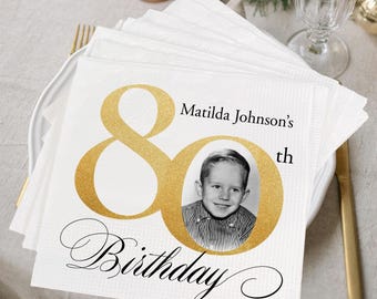 Puede incluir: Servilleta de papel blanca con un 80 dorado impreso en ella. El número 80 tiene una foto de un niño pequeño dentro. El texto "Matilda Johnson's 80th Birthday" está impreso debajo del número 80.