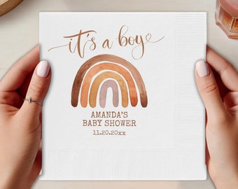 May include: White paper napkin with a brown and orange watercolour rainbow design. The text "it's a boy" is written in cursive above the rainbow. The text "Amanda's Baby Shower 11.20.20xx" is written below the rainbow.