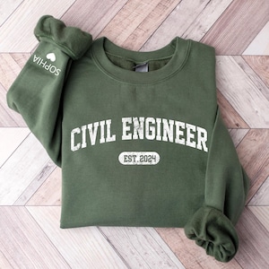 May include: A green sweatshirt with the text "CIVIL ENGINEER EST. 2024" in white. The sweatshirt has a white heart and the name "SOPHIA" on the left sleeve.