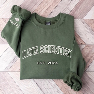 May include: A green sweatshirt with the text "DATA SCIENTIST EST. 2024" in white. The sweatshirt has a small heart with the word "Sophia" on the left sleeve.