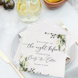 May include: A white card with green foliage and gold glitter accents. The text reads "Welcome to the night before celebrating Emily & Colton November 18, 2023".