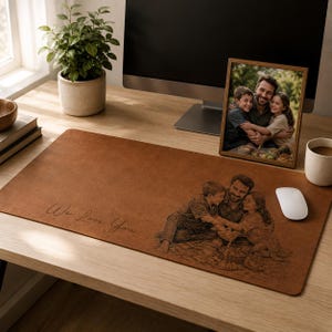 May include: A brown desk mat with the engraved phrase "We Love You" and a family portrait. A framed photo and a computer monitor are on the desk. A potted plant and a cup of coffee are also visible.
