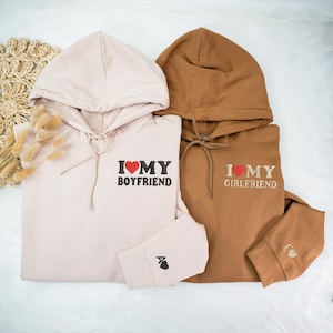 May include: Two hooded sweatshirts, one in light pink and one in brown, with embroidered hearts and the text "I love my boyfriend" and "I love my girlfriend".