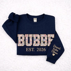 May include: A navy blue sweatshirt with the word "BUBBF" in a floral pattern across the chest. The text "EST. 2026" is below the word. The sleeve has the names "Daniel, Katie, Ethan" embroidered in gold with a heart.