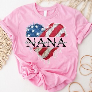 K&ouml;nnte beinhalten: Hellrosa T-Shirt mit einem herzf&ouml;rmigen Design, das die amerikanische Flagge und das Wort "NANA" in Schwarz zeigt. Unter dem Wort "NANA" stehen die Namen "Daniel", "Sophia" und "Ethan" in feiner Schrift.