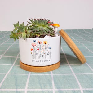 May include: White ceramic planter with a floral design and a wooden base. The planter contains a succulent plant, white pebbles, and a small mushroom figurine. The names "ETHAN & SOPHIA" and the date "07.07.2025" are printed on the planter.
