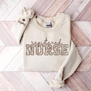 May include: A beige sweatshirt with the text "registered NURSE" in brown letters with a floral pattern.