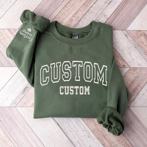 May include: A green sweatshirt with the word "CUSTOM" printed in white on the front. The sweatshirt has a crew neck and long sleeves.
