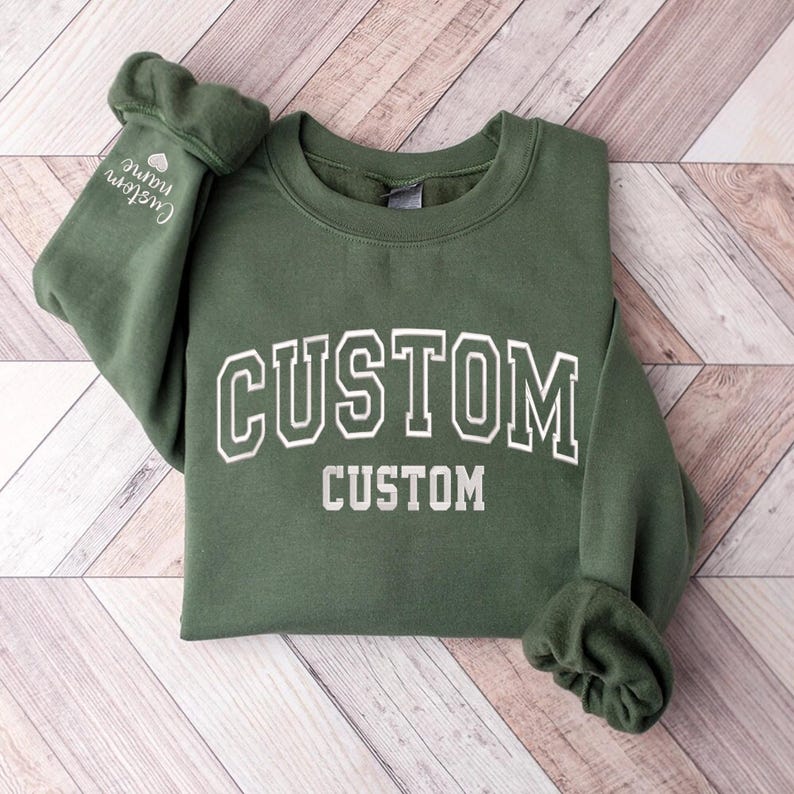 May include: A green sweatshirt with the word "CUSTOM" printed in white on the front. The sweatshirt has a crew neck and long sleeves.