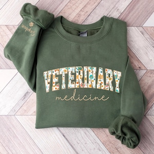 May include: A green sweatshirt with the text "VETERINARY medicine" in gold lettering. The word "VETERINARY" is decorated with a floral pattern.