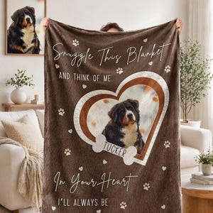 May include: A brown fleece blanket featuring a central heart-shaped frame containing a photo of a Bernese Mountain Dog. The blanket displays the text "Snuggle This Blanket AND THINK OF ME" and "In Your Heart I'LL ALWAYS BE" with a bone graphic labeled "TUCKER".