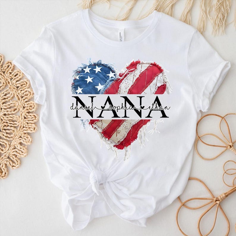 K&ouml;nnte beinhalten: Wei&szlig;es T-Shirt mit einem herzf&ouml;rmigen Design, das ein verblasstes amerikanisches Flaggenmuster zeigt. Das Design enth&auml;lt das Wort "NANA" und die Namen "Daniel, Sophia, Ethan". Das T-Shirt ist an der Taille geknotet.