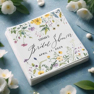 May include: White paper napkins with a floral design in shades of yellow, green, purple, and pink. The text "Sophia's Bridal Shower" and "April 17, 2025" is printed in black.