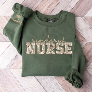 May include: A green sweatshirt with the text "registered NURSE" in gold lettering with a floral pattern. The word "NURSE" is in large letters.