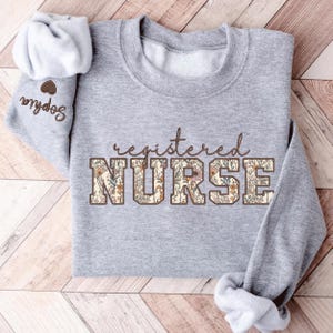 May include: A gray sweatshirt with the text "registered NURSE" in brown letters with a floral pattern. The letters are outlined in brown.