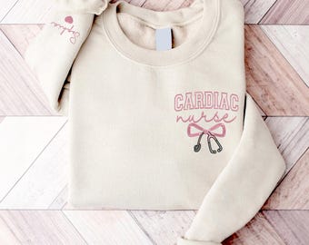May include: A cream-colored sweatshirt with the text "CARDIAC nurse" in pink and a pink stethoscope bow.