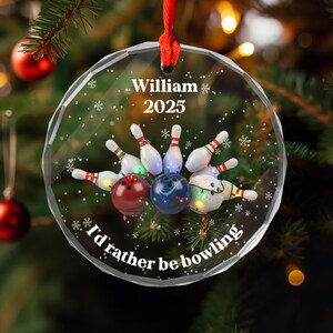 May include: A clear, round Christmas ornament with a red ribbon. The ornament features a bowling theme with bowling pins, bowling balls, and the text "William 2025" and "I'd rather be bowling."