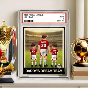 May include: A framed print featuring a soccer-themed illustration. The image shows a father and two children in red and white soccer uniforms, with the text "DADDY'S DREAM TEAM." The frame includes text: "2025 FAMILY LEAGUE NO. 1 DAD."