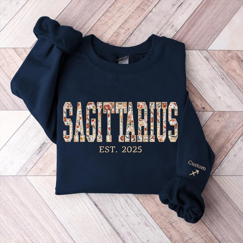 May include: Navy blue sweatshirt with a floral Sagittarius design and the text "EST. 2025". The sweatshirt has a custom Sagittarius symbol embroidered on the sleeve.