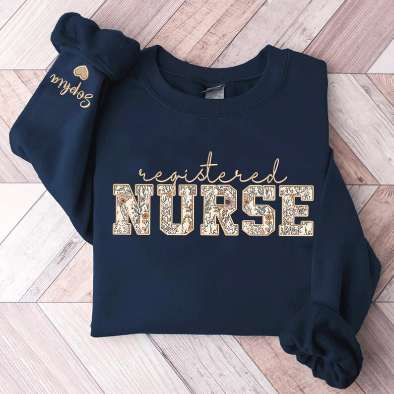 May include: Navy blue sweatshirt with the text "registered NURSE" in white letters with a floral pattern. The text is in a varsity style font.