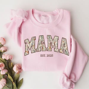 May include: Pink sweatshirt with a floral print "MAMA" graphic and the text "EST. 2025" below.