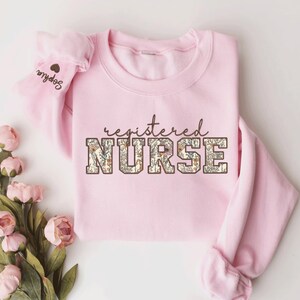 May include: Pink sweatshirt with the text "registered NURSE" in brown letters with a floral pattern. The letters are outlined in brown.