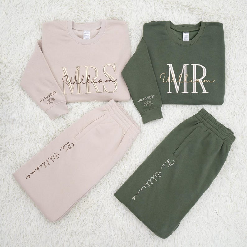 May include: Matching beige and olive green loungewear sets. Each set includes a crewneck sweatshirt and sweatpants. The sweatshirts are embroidered with "MRS" and "MR" with the last name "William" in gold lettering. The date "09.19.2025" is on the sleeves.