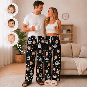May include: Black pajama pants featuring a repeating pattern of white stars, small baby faces, and the text "BEST DAD EVER" or "BEST MOM EVER". The pants have a white drawstring waist. The design includes three circular photo inserts of a baby.