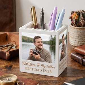 May include: A white square desk organizer with a building block texture on the top rim. The front features a photo of a man holding a camera with the text "With Love, To My Father BEST DAD EVER" printed below. A side panel shows a photo of a man.