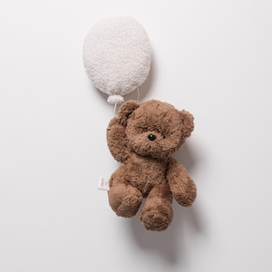 Pode incluir: Um urso de pel&uacute;cia marrom segurando um bal&atilde;o branco e fofo. O urso tem uma pequena etiqueta anexada. O brinquedo est&aacute; em um fundo branco liso.