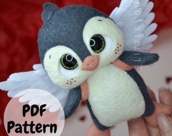 May include: A PDF pattern for a felt penguin with white wings. The penguin is wearing a white and gray outfit and has large, black eyes. The pattern is available for download.  PDF Pattern