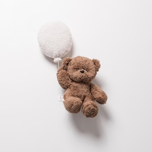 Pode incluir: Um urso de pel&uacute;cia marrom segurando um bal&atilde;o branco e fofo. O urso tem um pequeno nariz preto e &eacute; feito de material macio e texturizado. O bal&atilde;o &eacute; redondo e tamb&eacute;m tem uma apar&ecirc;ncia macia e texturizada. O fundo &eacute; branco liso.