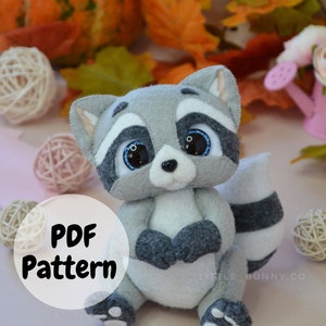 May include: A PDF pattern for a cute gray and white raccoon plush toy. The pattern includes instructions for sewing the toy and is available for download. The image shows the finished plush toy sitting on a pink surface with fall leaves and pumpkins in the background.