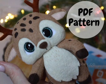 May include: A brown and white felt reindeer plush toy with large eyes and a brown antler. The toy is being held in a hand. The text "PDF Pattern" is written in a white circle on a gray background.