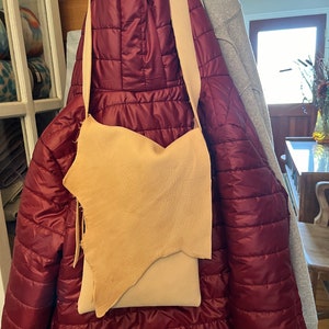 May include: A light brown leather crossbody bag with a long strap hanging from a red quilted jacket.