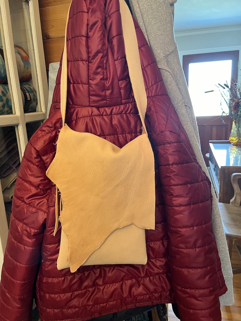 May include: A light brown leather crossbody bag with a long strap hanging from a red quilted jacket.