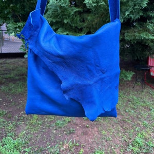 May include: A bright blue leather shoulder bag with a flap closure. The bag is made of a soft, supple leather and has a casual, relaxed style.