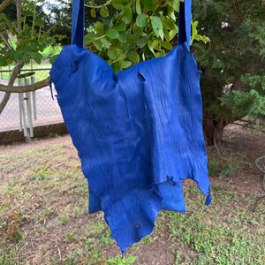 May include: A blue leather bag with a strap hanging from a tree branch. The bag has a distressed look with holes and frayed edges.