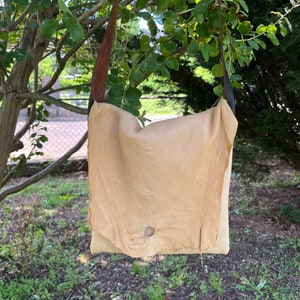 May include: A light brown leather crossbody bag with a brown and black strap. The bag has a single hole in the front.